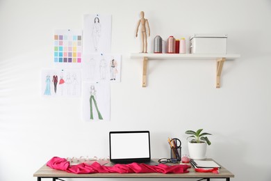 Photo of Fashion designer`s workplace with laptop, sketches of new outfits and other supplies