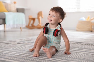 Photo of Cute little baby with headphones on floor at home