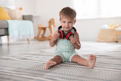 Photo of Cute little baby with headphones on floor at home