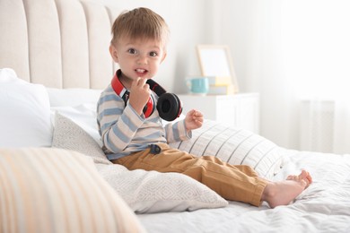 Cute little baby with headphones on bed at home