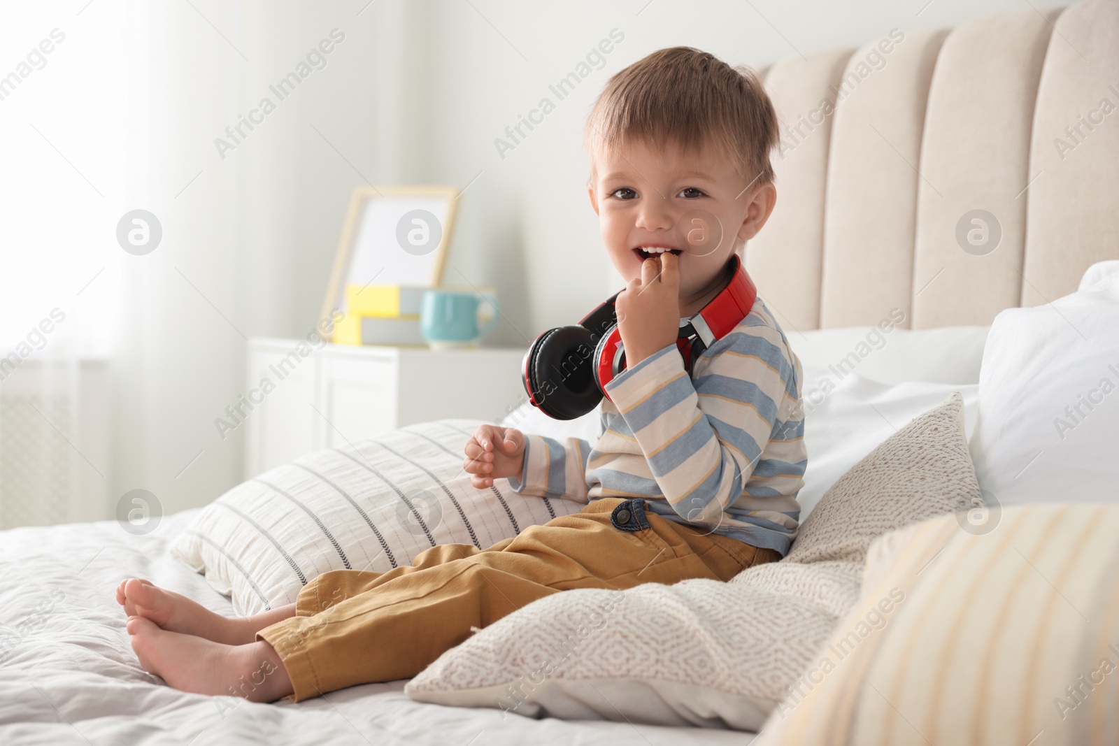 Photo of Cute little baby with headphones on bed at home