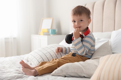 Cute little baby with headphones on bed at home