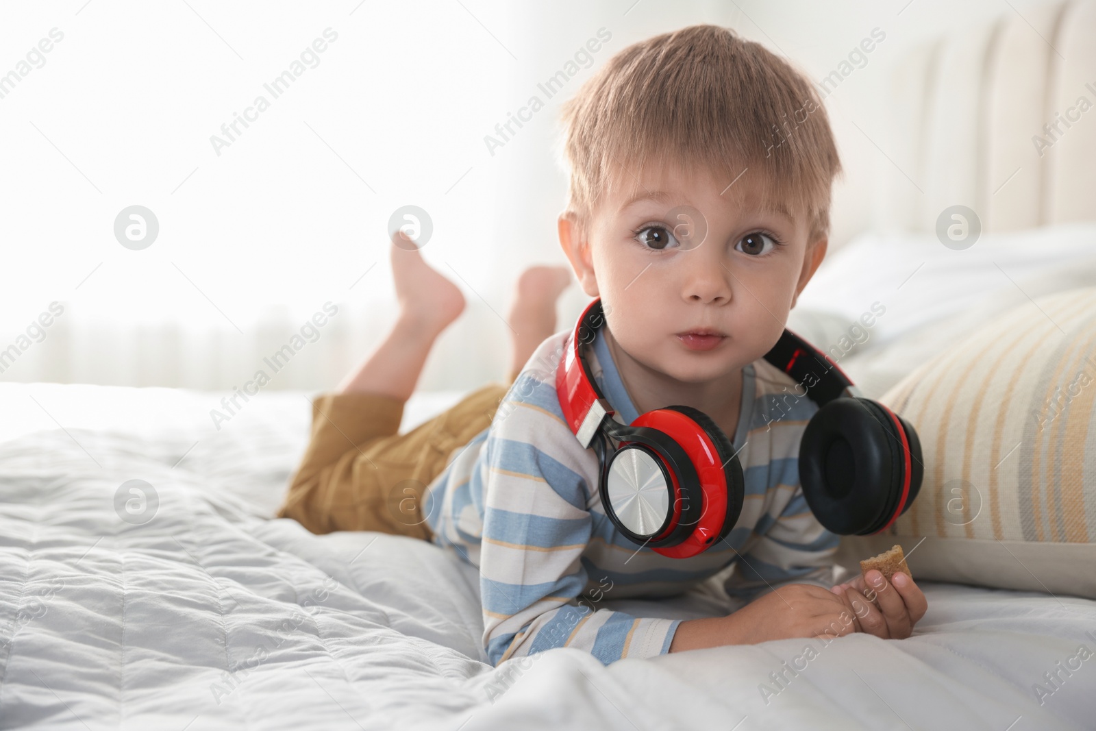 Photo of Cute little baby with headphones on bed at home