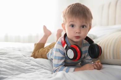 Cute little baby with headphones on bed at home