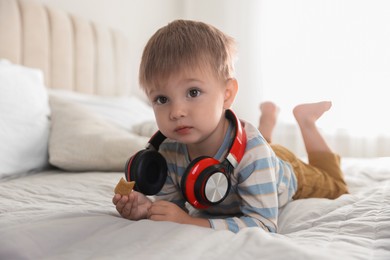 Cute little baby with headphones on bed at home