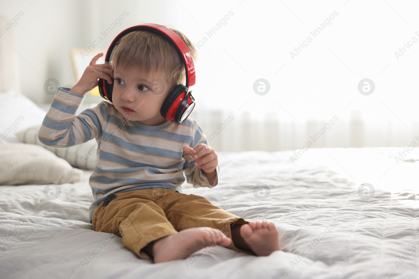 Photo of Cute little baby in headphones on bed at home, space for text