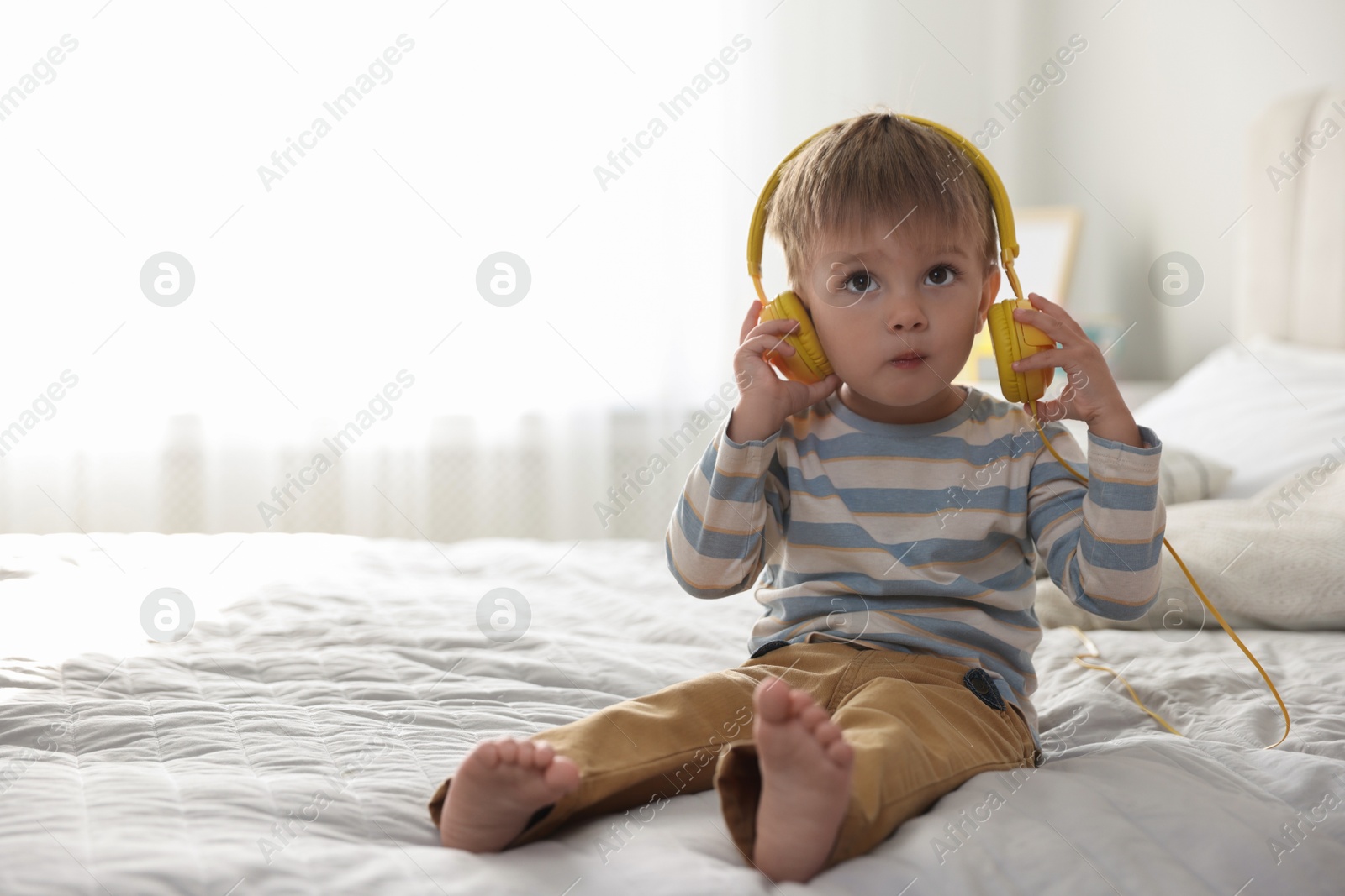 Photo of Cute little baby in headphones on bed at home, space for text