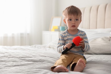 Photo of Cute little baby with microphone on bed at home, space for text