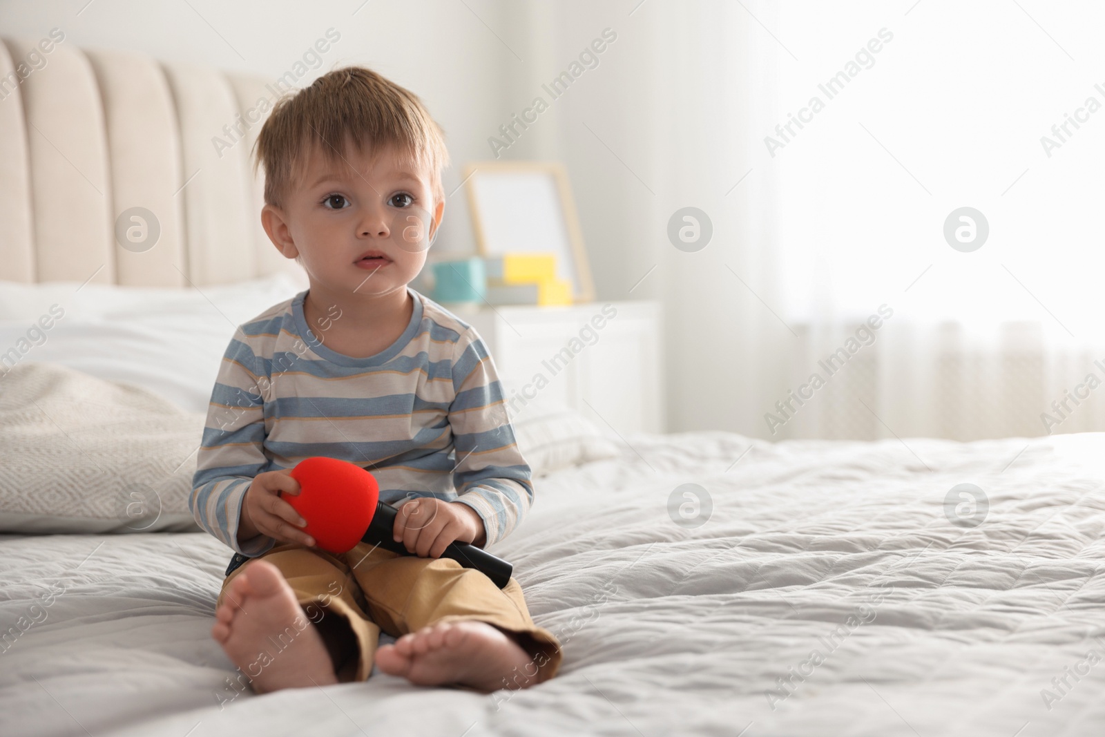 Photo of Cute little baby with microphone on bed at home, space for text