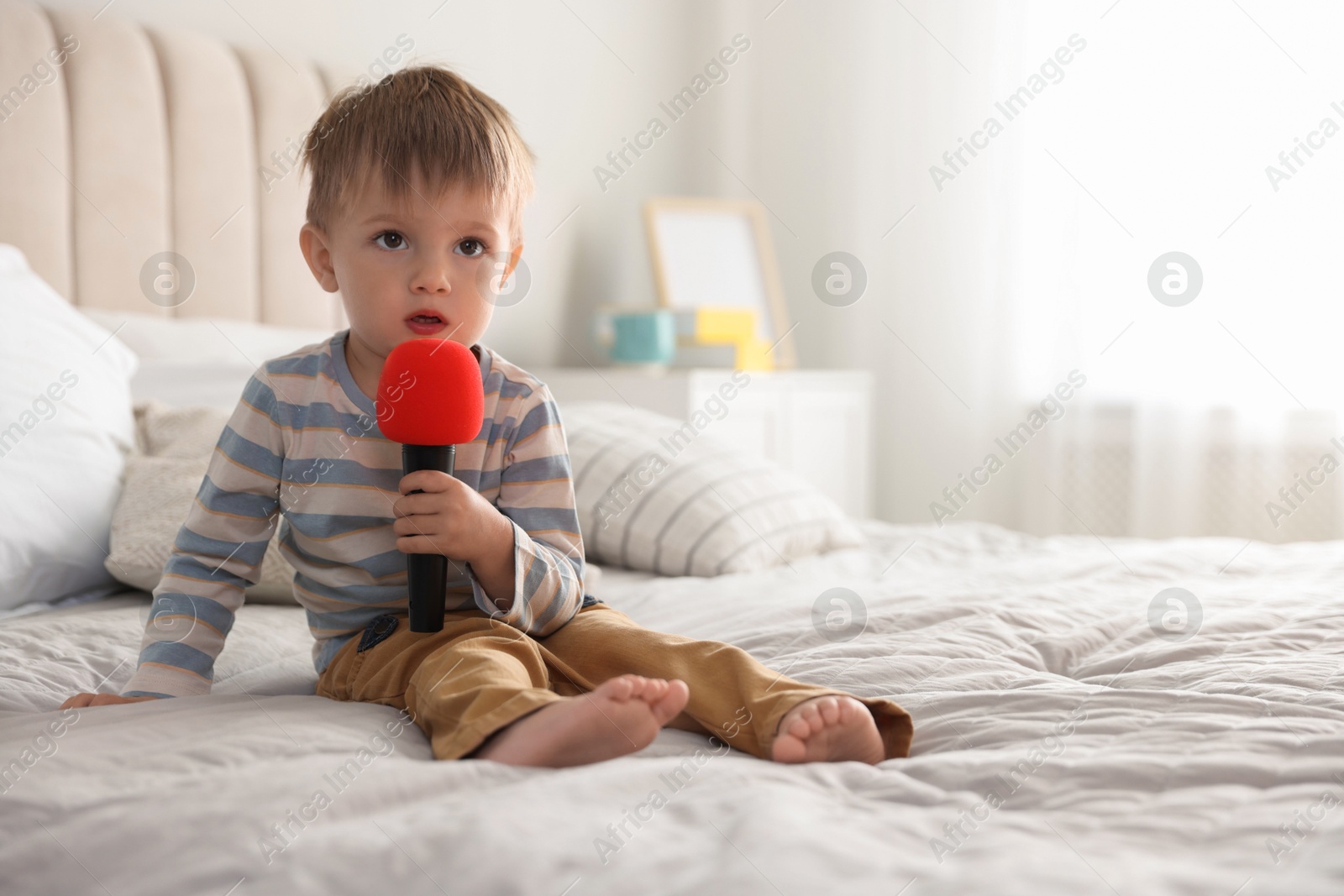 Photo of Cute little baby with microphone on bed at home, space for text