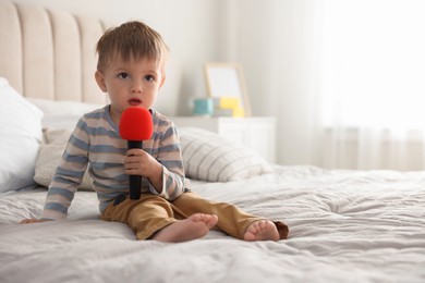 Cute little baby with microphone on bed at home, space for text