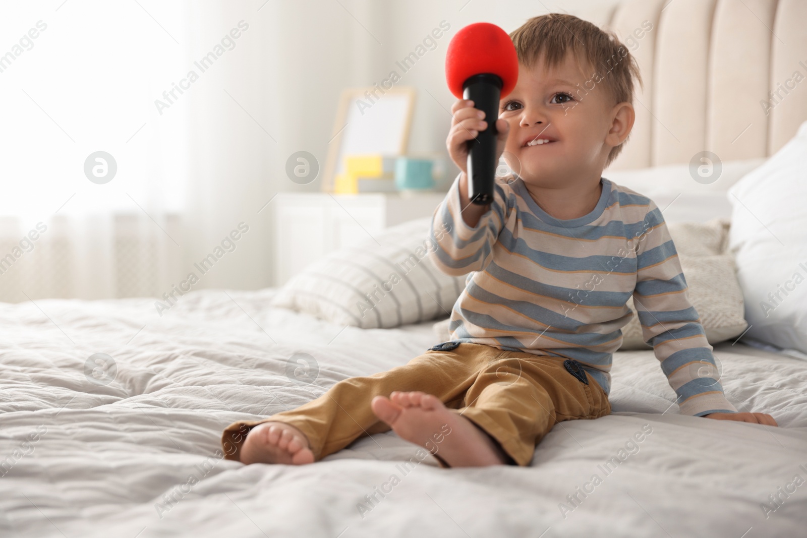 Photo of Cute little baby with microphone on bed at home, space for text