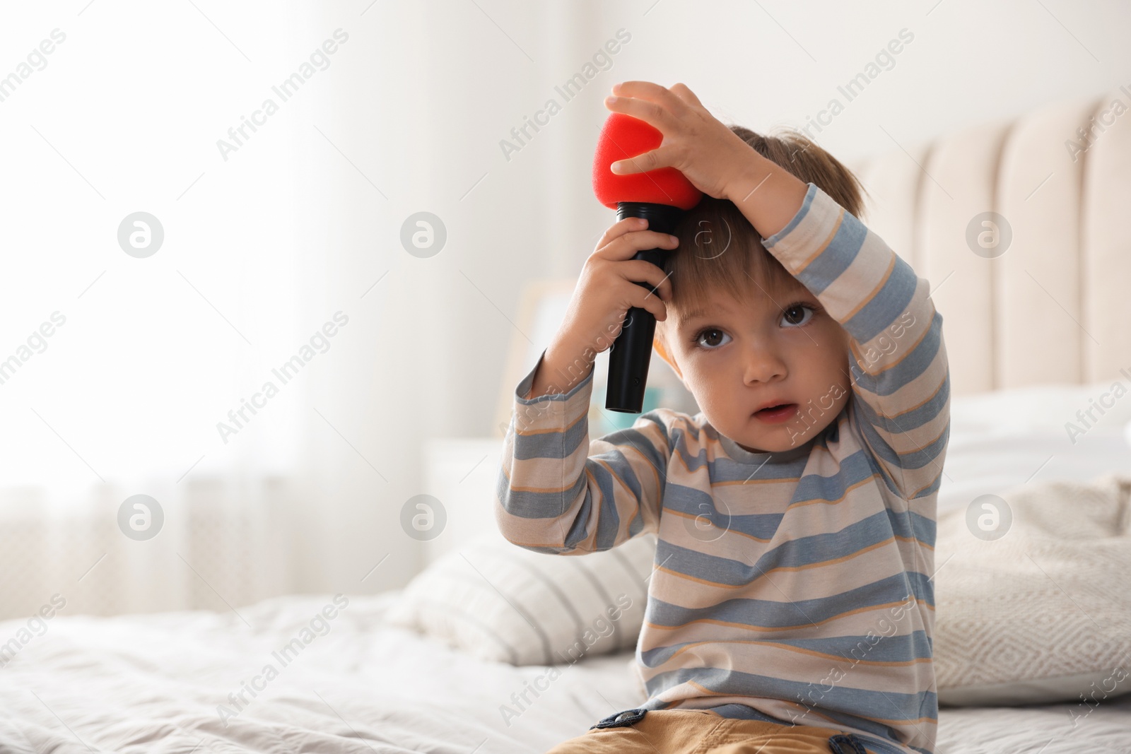 Photo of Cute little baby with microphone on bed at home, space for text