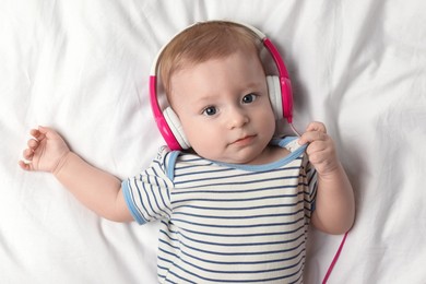 Cute little baby with headphones lying on bed, top view