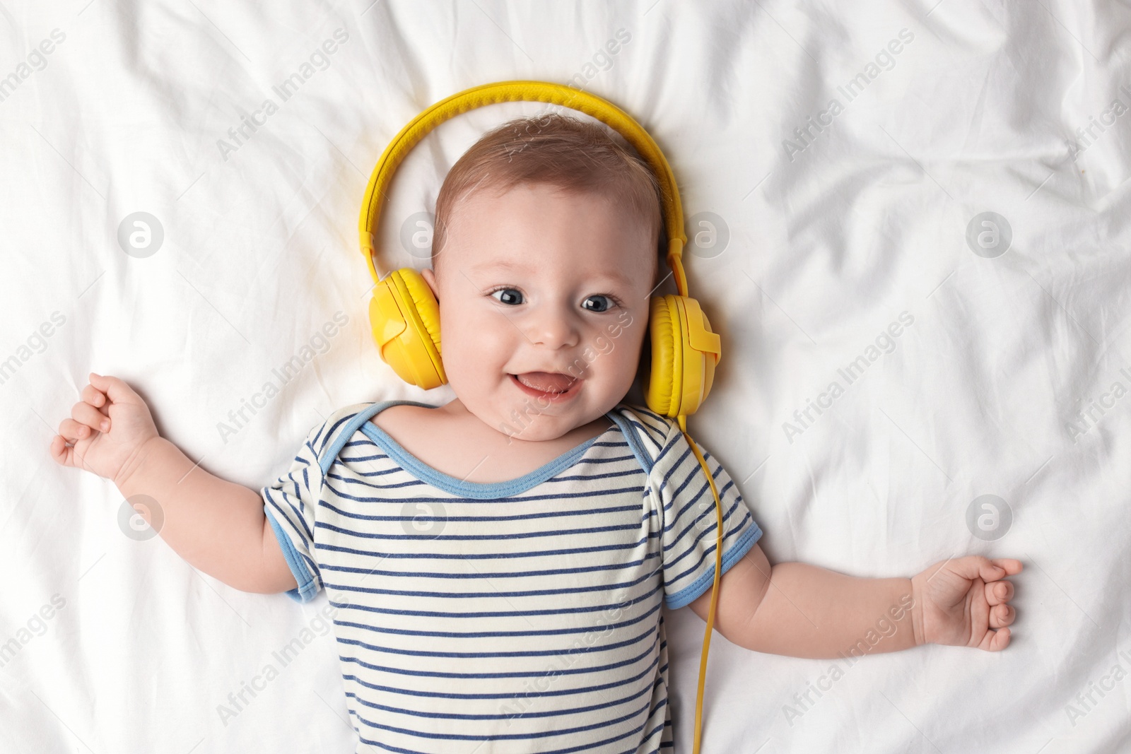 Photo of Cute little baby with headphones lying on bed, top view