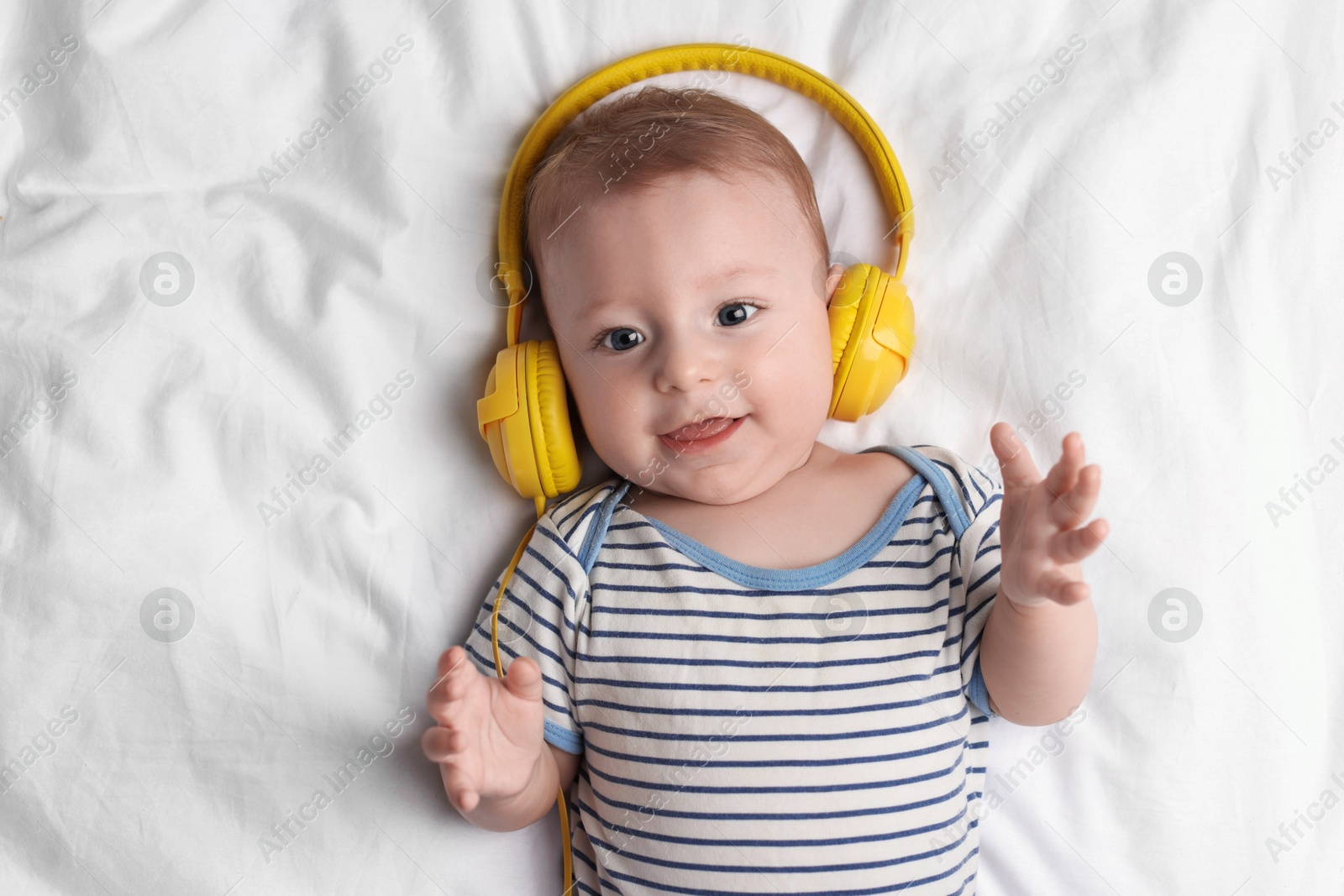 Photo of Cute little baby with headphones lying on bed, top view