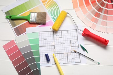 Photo of Designer's workplace with color palettes, floor plan and different supplies on white wooden table, flat lay