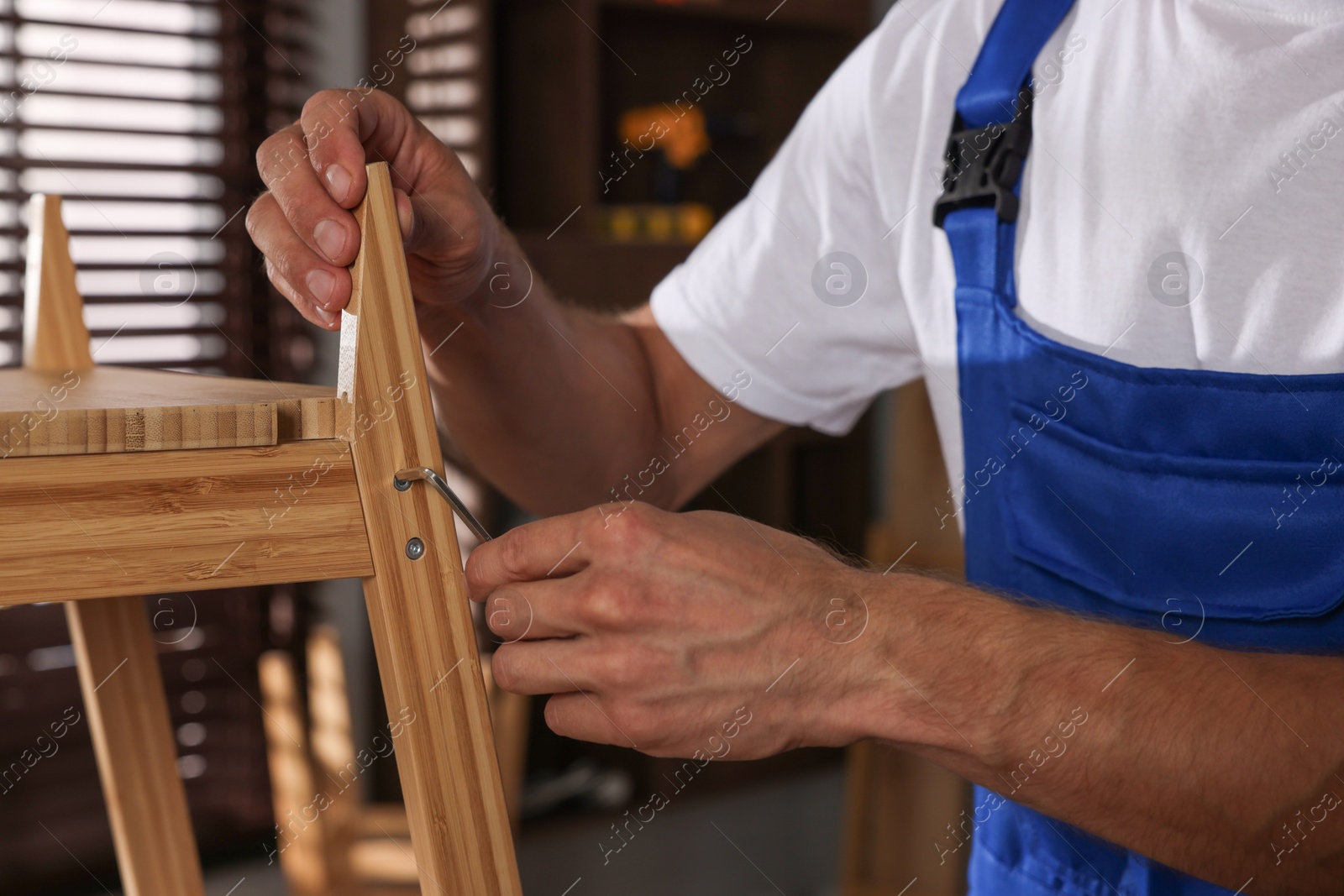 Photo of Man in uniform repairing wooden stool indoors, closeup