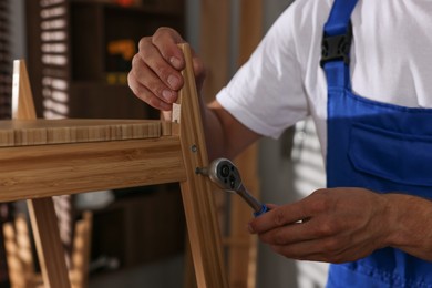 Photo of Man repairing wooden stool with torque wrench indoors, closeup