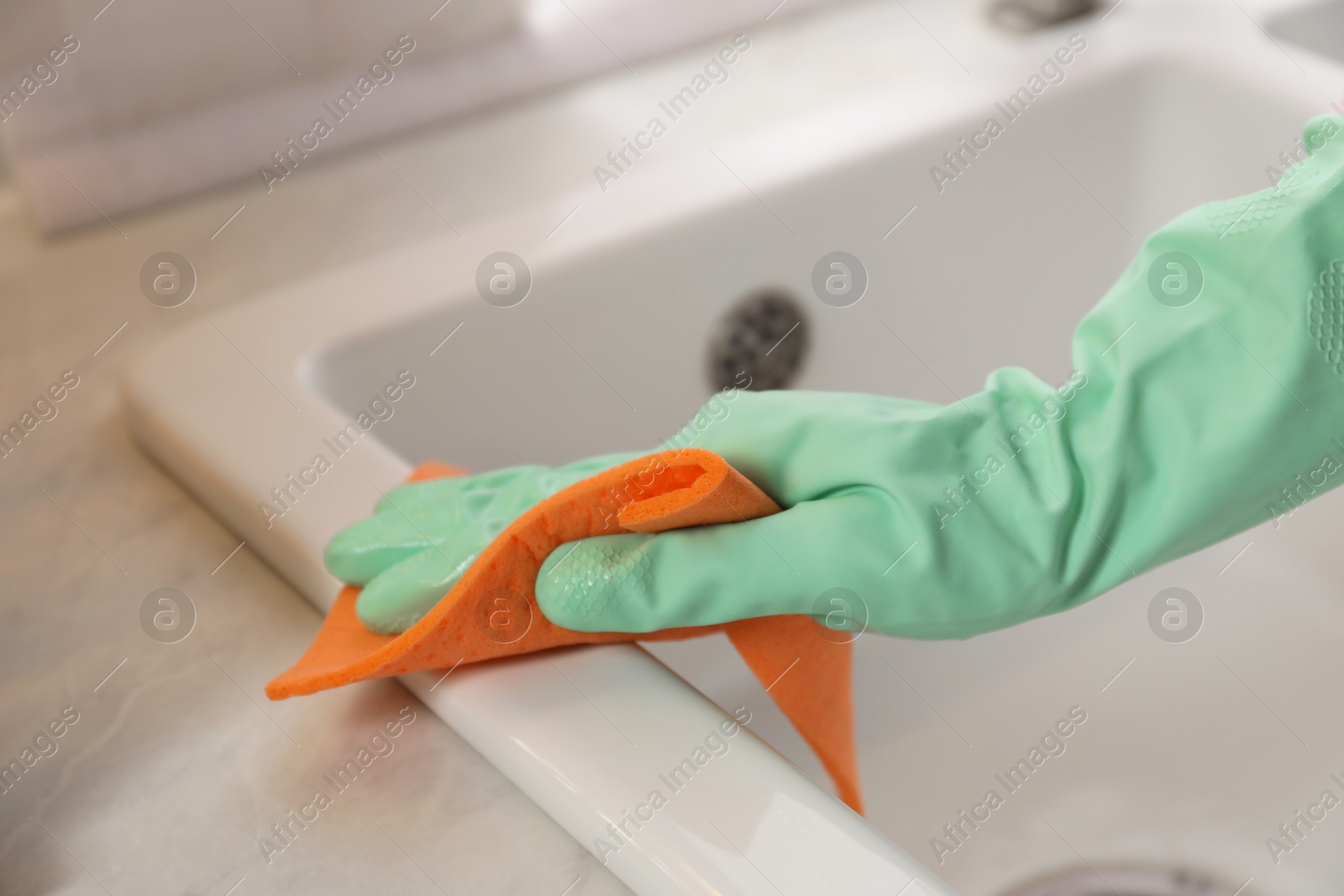 Photo of Woman wiping sink with napkin in kitchen, closeup