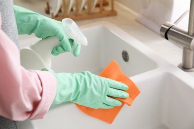 Photo of Woman spraying detergent onto napkin in kitchen, closeup. Cleaning sink