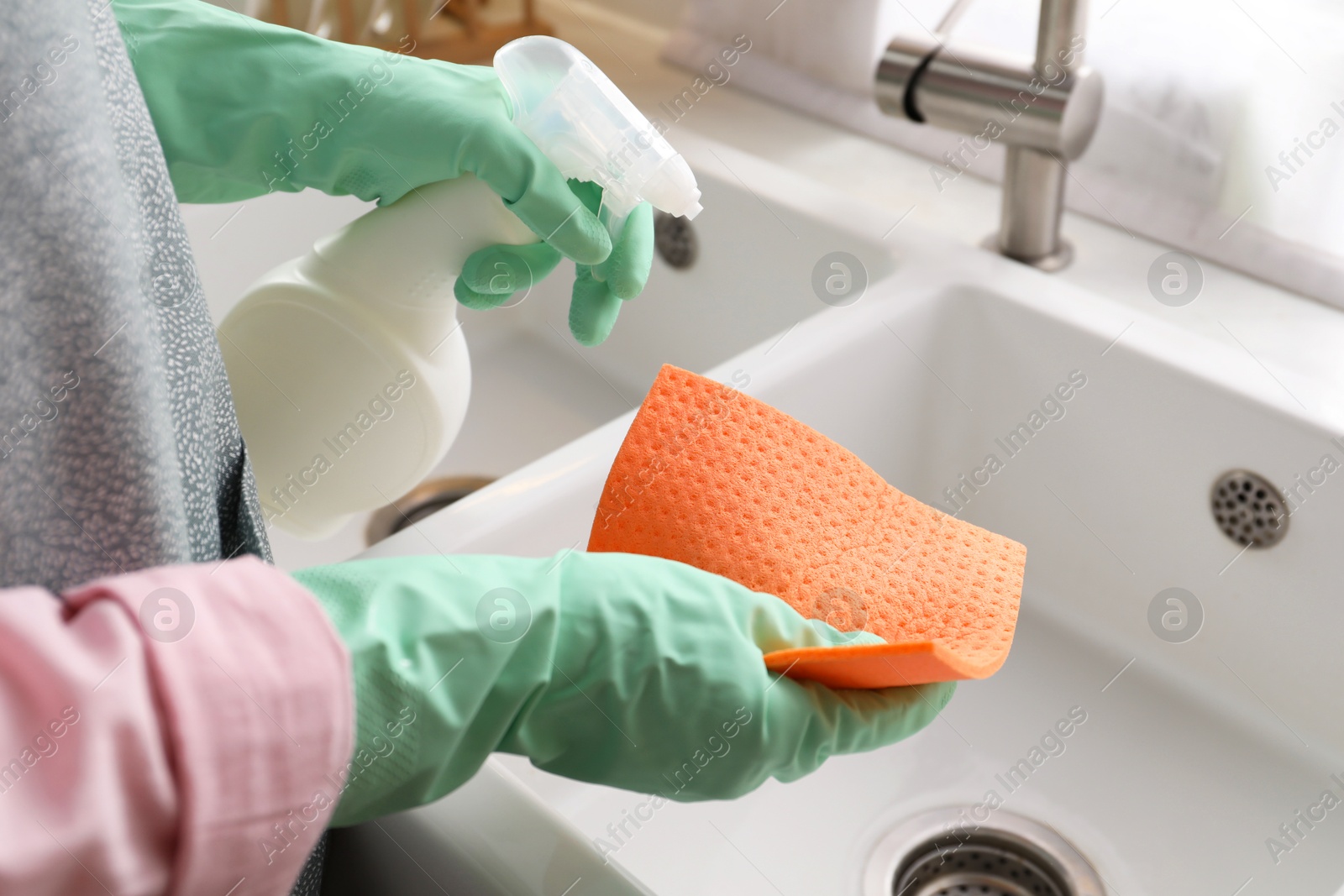 Photo of Woman spraying detergent onto napkin in kitchen, closeup. Cleaning sink