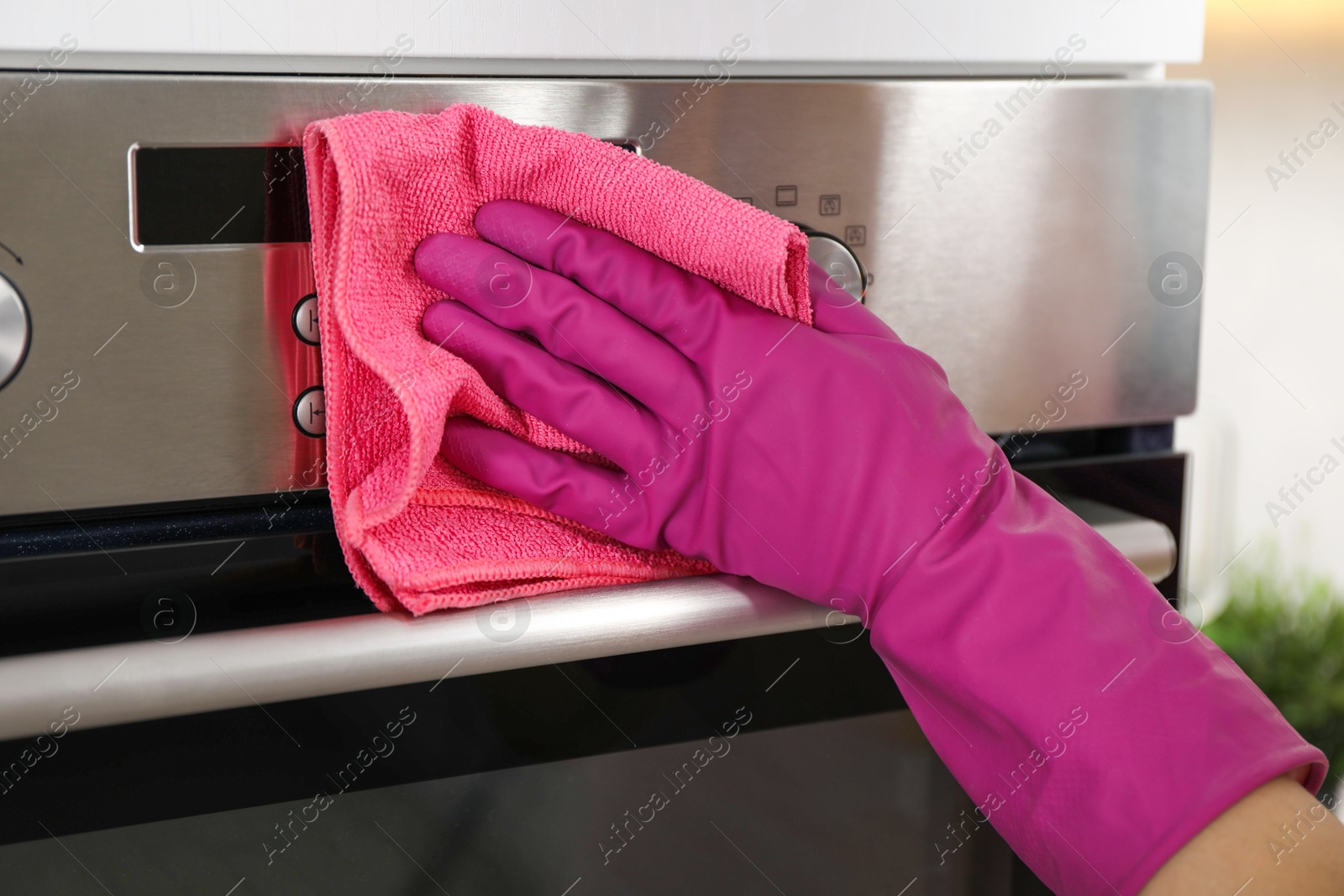 Photo of Woman wiping electric oven with rag in kitchen, closeup