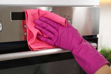 Photo of Woman wiping electric oven with rag in kitchen, closeup