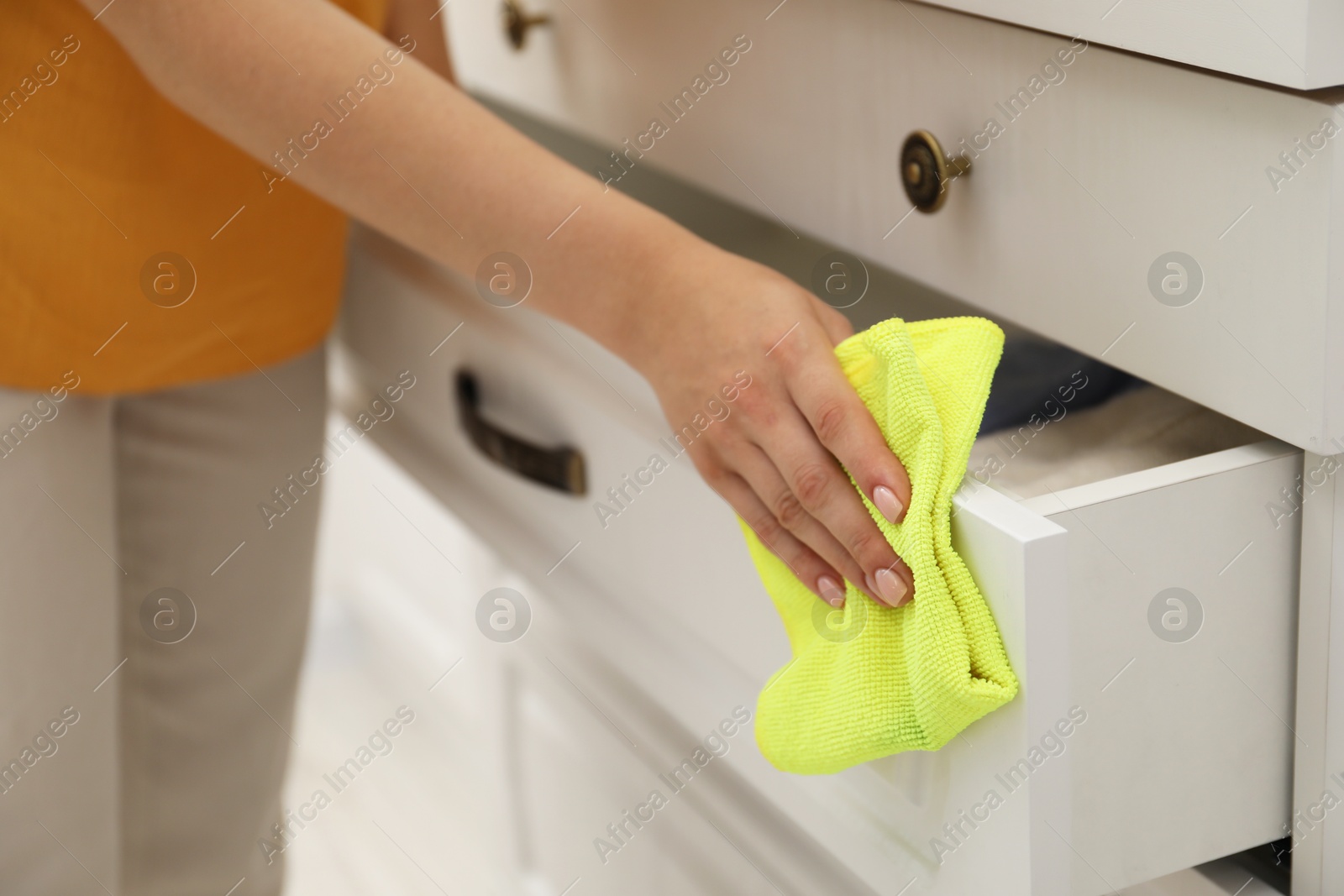 Photo of Woman wiping chest of drawers with rag indoors, closeup