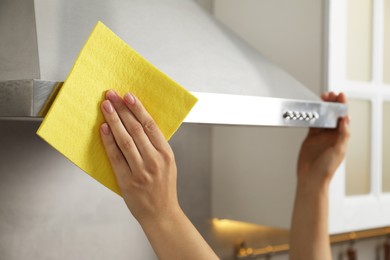 Photo of Woman cleaning kitchen hood with napkin at home, closeup