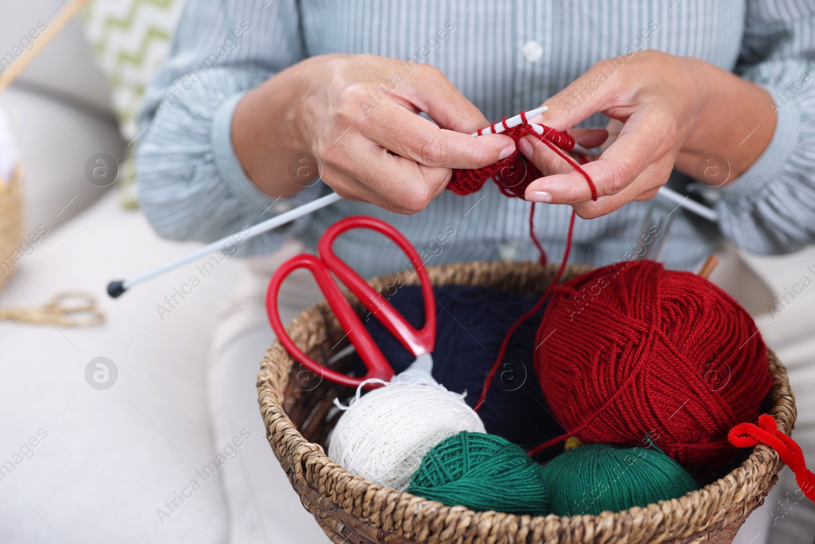 Photo of Woman with basket of yarn knitting at home, closeup