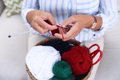 Photo of Woman with basket of yarn knitting at home, closeup