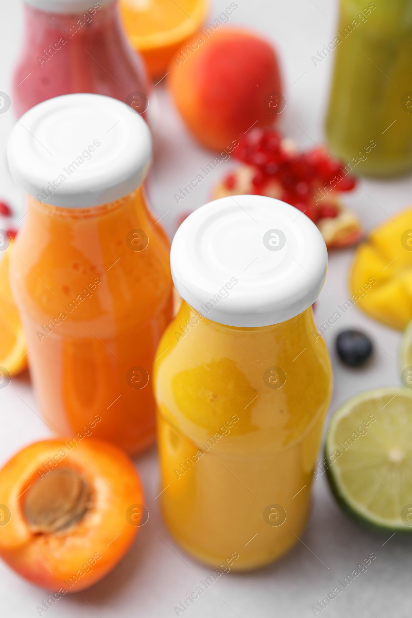 Photo of Glass bottles of tasty smoothies and different products on white table, closeup