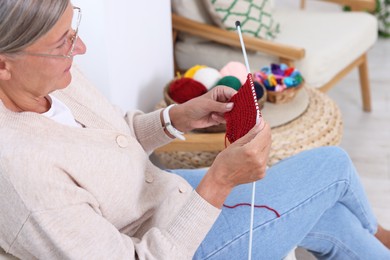 Photo of Senior woman with knitting needles looking at pattern at home