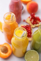 Glass bottles of tasty smoothies and different products on white table, closeup