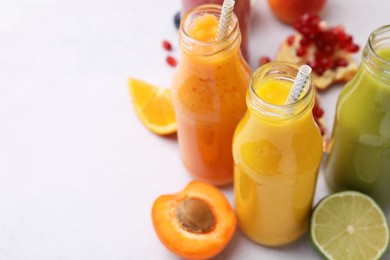 Photo of Glass bottles of tasty smoothies and different products on white table, closeup. Space for text