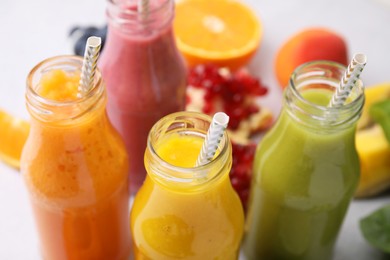 Glass bottles of tasty smoothies and different products on white table, closeup