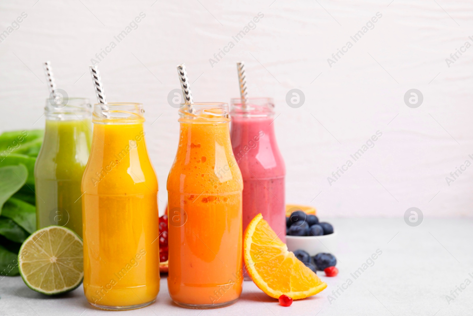 Photo of Glass bottles of tasty smoothies and different products on white table, space for text