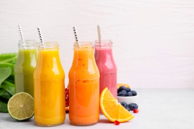 Glass bottles of tasty smoothies and different products on white table, space for text