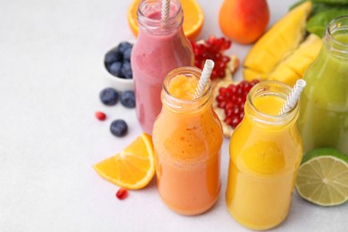 Photo of Glass bottles of tasty smoothies and different products on white table, closeup. Space for text