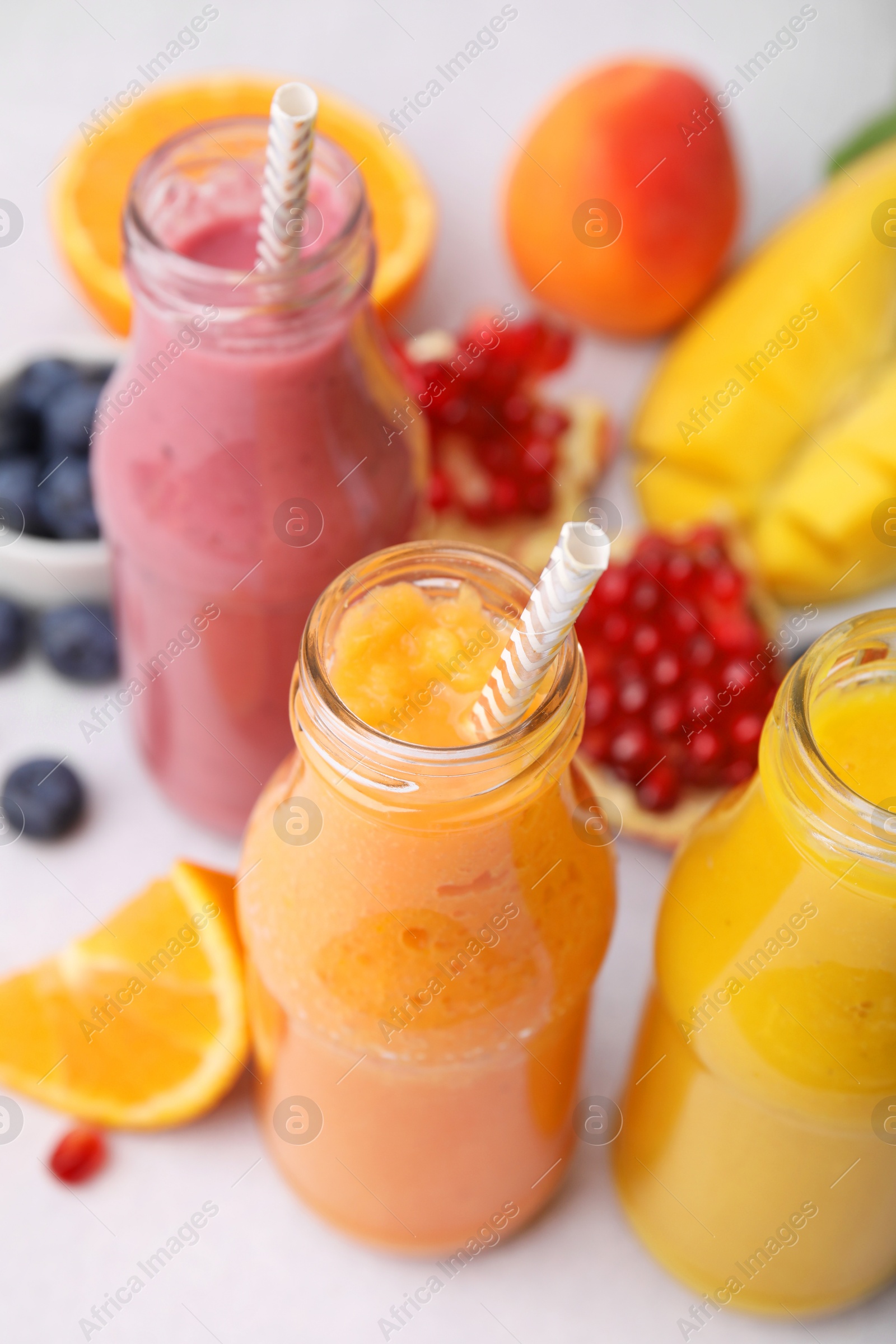 Photo of Glass bottles of tasty smoothies and different products on white table, closeup