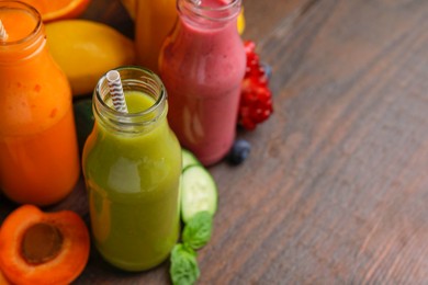 Glass bottles of tasty smoothies and different products on wooden table, closeup. Space for text