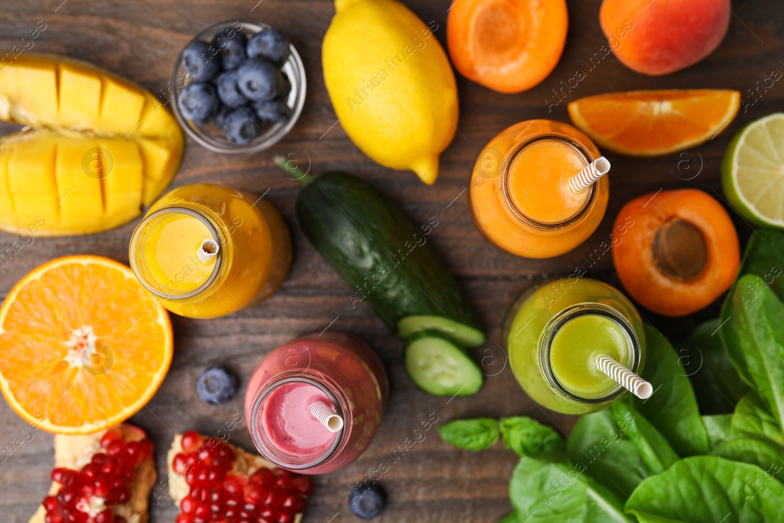 Photo of Glass bottles of tasty smoothies and different products on wooden table, flat lay