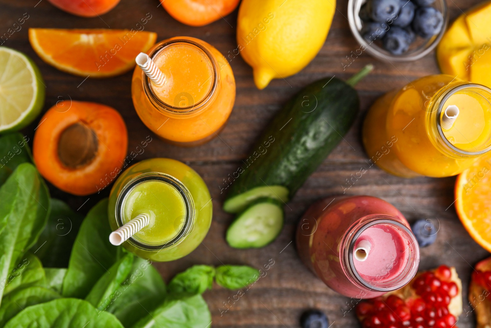 Photo of Glass bottles of tasty smoothies and different products on wooden table, flat lay