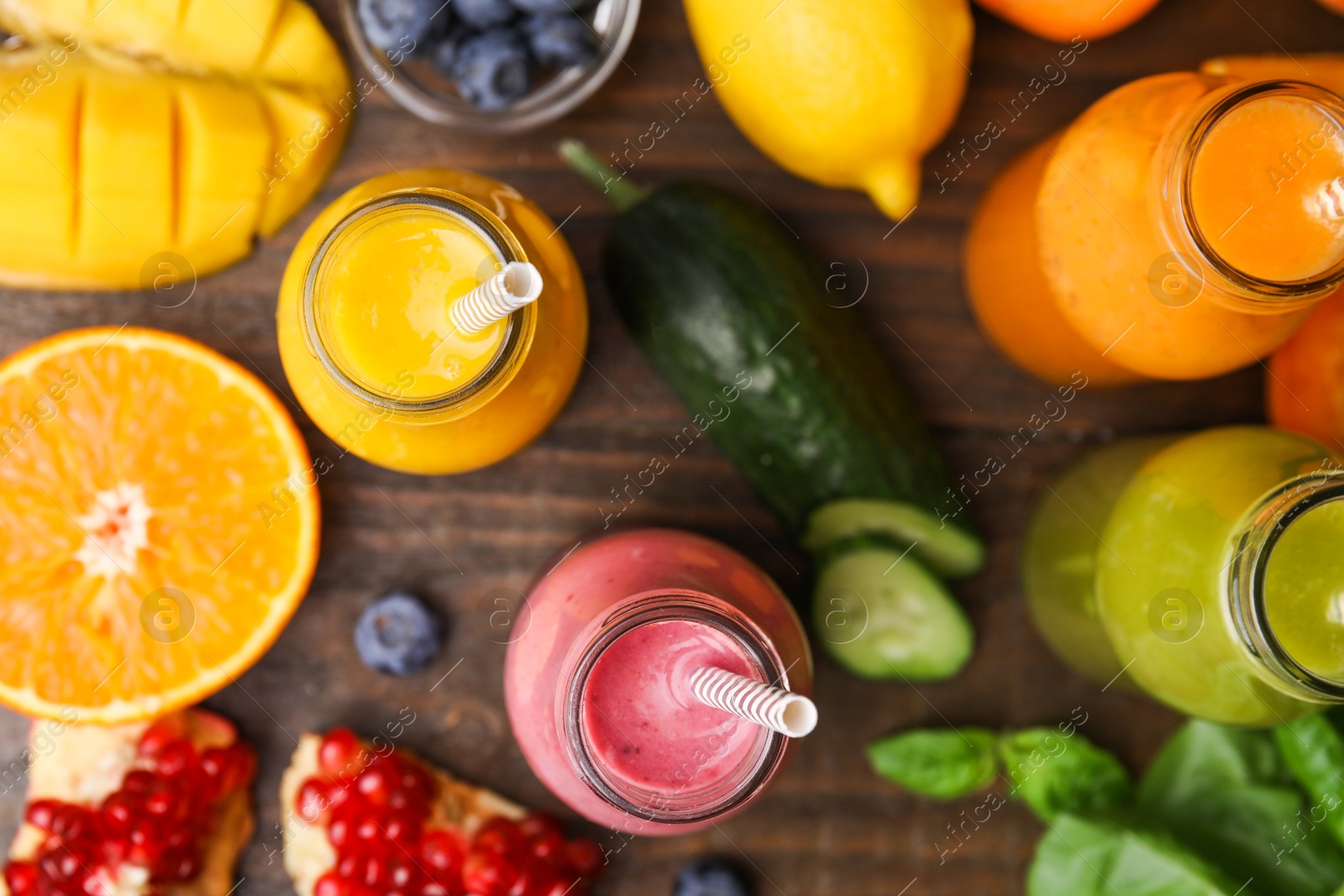 Photo of Glass bottles of tasty smoothies and different products on wooden table, flat lay