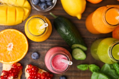 Glass bottles of tasty smoothies and different products on wooden table, flat lay