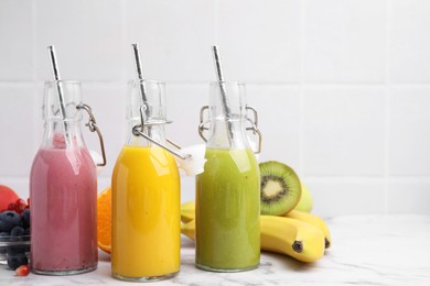 Photo of Glass bottles of tasty smoothies and different products on white marble table, space for text