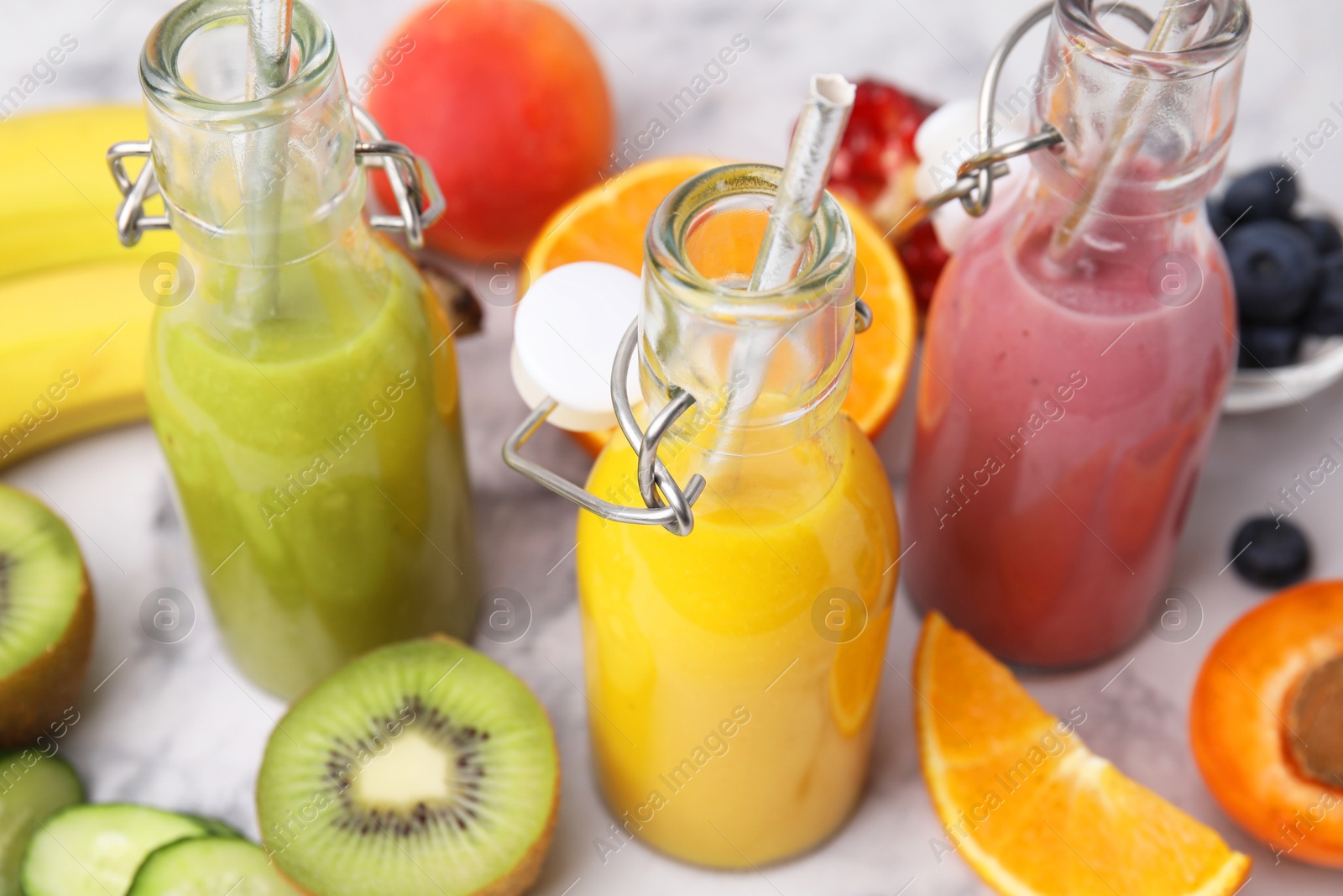 Photo of Glass bottles of tasty smoothies and different products on white marble table, closeup