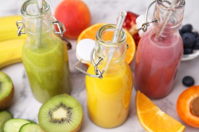 Photo of Glass bottles of tasty smoothies and different products on white marble table, closeup