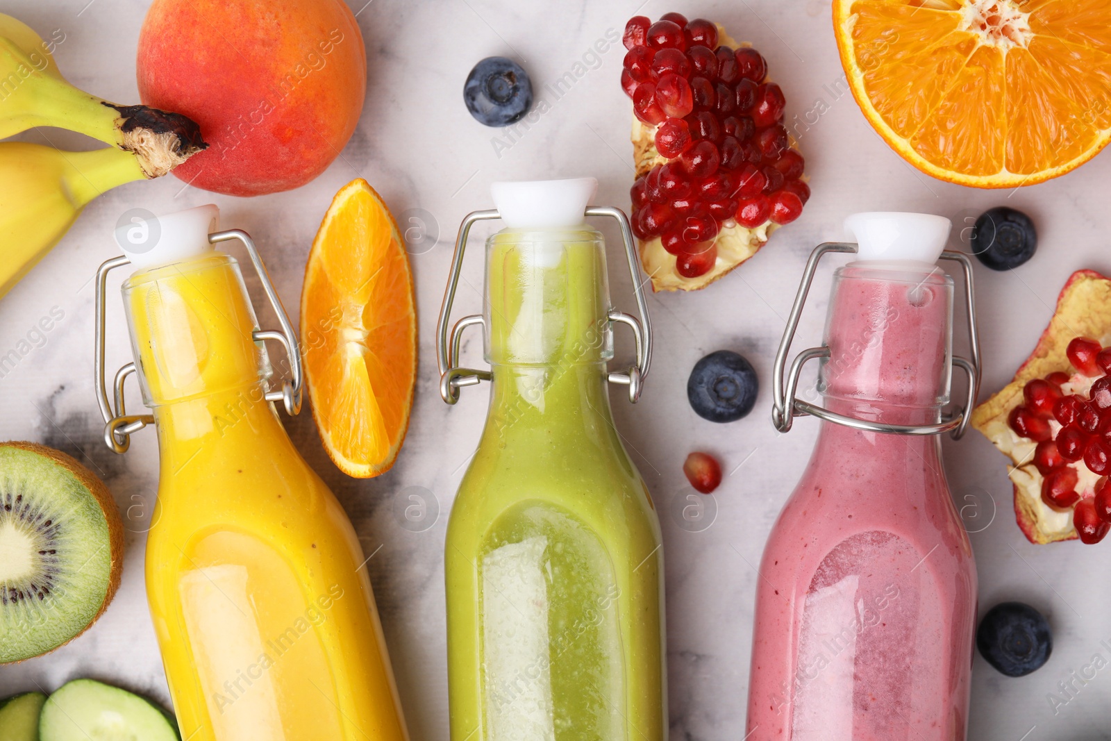 Photo of Glass bottles of tasty smoothies and different products on white marble table, flat lay